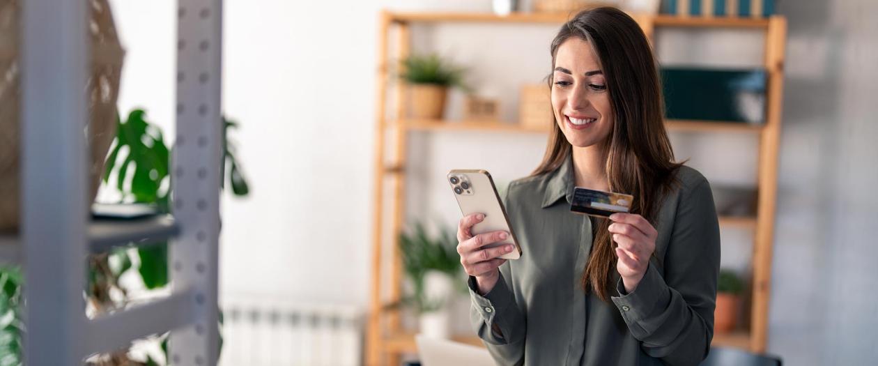 Smiling woman holding credit card and looking at cell phone