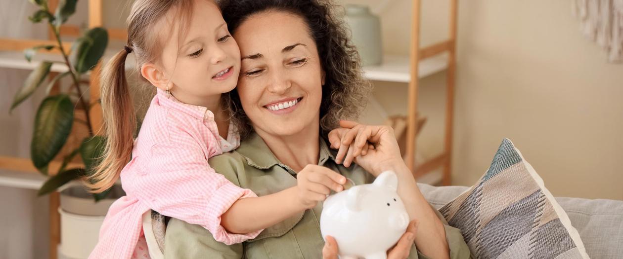 mom and daughter putting money in piggy bank